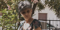 Brustbild einer Frau mit Sonnenbrille und kurzen grauen Haaren in einem Garten
