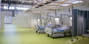 Leere Krankenhausbetten und Trennwände stehen in einer großen Halle mit Blechdach