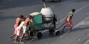 Bauarbeiter ziehen einen Zementmischer über die Straße
