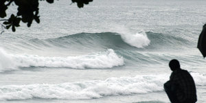 Mann hockt am Strand, an dem sich eine hohe Welle bricht