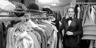 Schwarzweißaufnahme von Pierre Cardin in anzug und mit Fliege in einer Garderobe stehend, Kleider hängen von der Stange