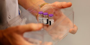 Eine medizinische Fachkraft hält einen transparenten Behälter mit lediglich 3 Impfdosen in den Händen