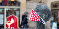 Statue mit einer roten Stoffmaske mit Punkten vor einer Apotheke