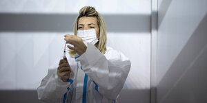 Eine Frau in Schutzkleidung und mit Mundschutzmaske zieht eine Spritze auf