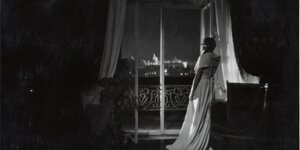 Szene aus dem Film „Tagebuch der Geliebten“: Eine Frau im Nachthemd lehnt mit dem Rücken zur Kamera an einem Fenster und blickt hinaus