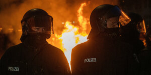 Zwei Polizisten mit Helmen stehen vor einem brennenden Mülleimer