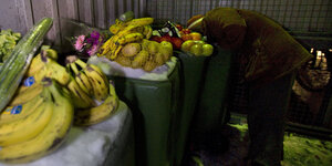 Bananen und Kartoffeln, Gurken liegen auf schneebedekcten Mülltonnen. Dahinter sucht ein Mensch nach weiterem Essen