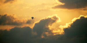 wolkiger Himme, mit schönem orangenem Sonnenuntergang, im Vordergrund ein fliegender Heißluftballon