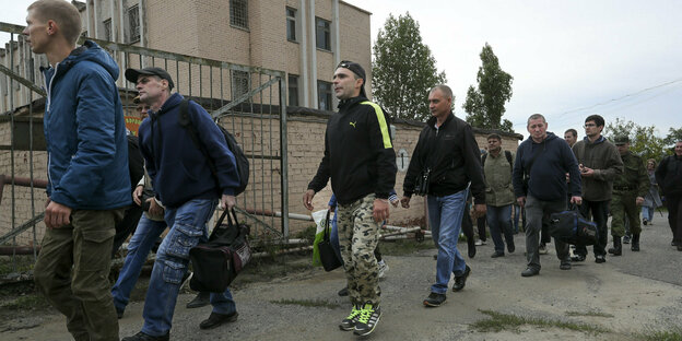 Eine Gruppe von etwa zehn Männern in Zivilkleidung, teils mit Reisetaschen in der Hand, läuft an einem Gebäude vorbei. Laut Bildbeschreibung ein Rekrutierungszentrum in Wolgograd.