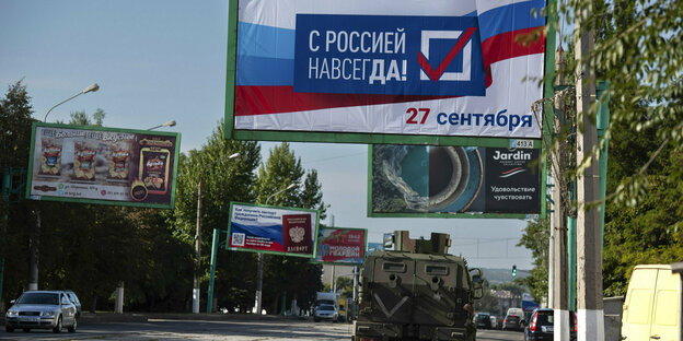Ein Militärfahrzeug fährt vor einem Wahlplakat, auf dem "Mit Russland für immer" steht