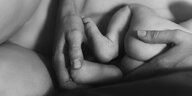 Ein Hände einer nackten Person halten schützend die Hände um ein nacktes Baby
