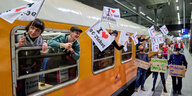 Fähnen mit Herzen und dem Wunsch nach einem 9 Euro Ticket werden von gut gelaunten Leuten aus einem Zugfenster gehängt