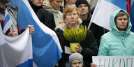 Eine Frau hält einen blau-gelben Blumentopf, sie ist von estnischen Fahnen umgeben