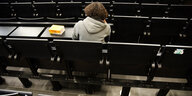 Junger Mensch von hinten in einem Hörsaal mit schwarzen Stühlen