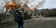 Ein Mann läuft an brennenden Häusern vorbei