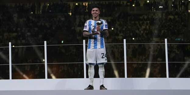 Fußballer Enzo Fernandez mit einer Trophäe auf der Bühne des WM-Finalstadions
