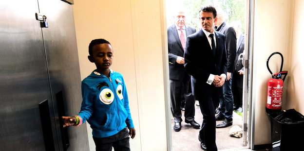 Premier Valls kommt durch die Tür. Im Gang steht ein kleiner Junge.