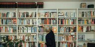 Vollgesopftes Bücherregal vor dem eine Frau steht, die Bücher einsortiert