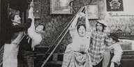 Eine altes schwarzweißes Filmbild, fünf Figuren in einer Wohnung, skurriles Durcheinander