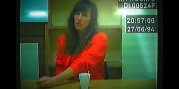 Video-Still einer Frau, die an einem Tisch sitzt