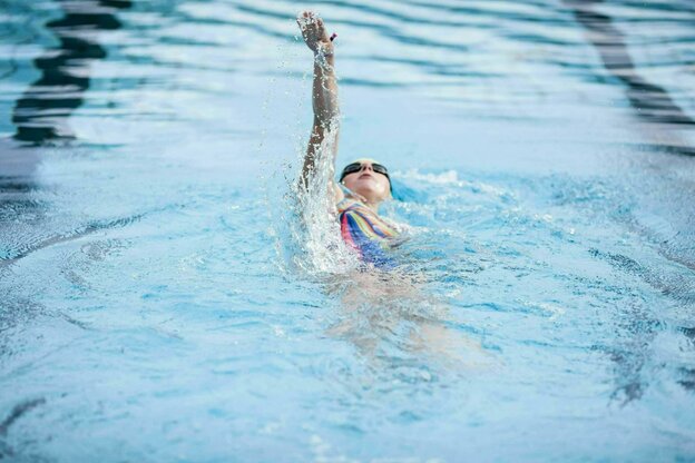 Eine junge Frau beim Rückenschwimmen in enem Schwimmbecken im Freibad