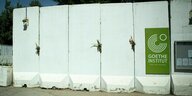 Helle Betonmauer in Kabul, die das Goetheinstitut vor Anschlägen schützen soll. Darauf ein grünes Schild, auf dem "Goethe Institut" steht.