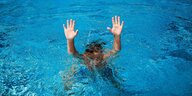 Kind taucht im Schwimmbad ab und hält die Hände in die Höhe