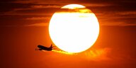 Die Sonne glüht an einem knall-orangen Himmel, davor fliegt ein Flugzeug vorbei.
