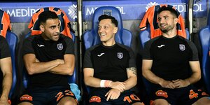 Mesut Özil sitzt mit seinen Spielerkollegen auf der Bank und lacht