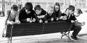 Mehrere Kinder auf eine Parkbank mit Smartphones.