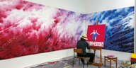 Der Maler Sun Mu sitz mit dem Rücken zum Bild an einer Staffelei und malt ein rotes Gemälde mit zwei Figuren. Ein Mann und eine Frau sind in Blau und Weiß gekleidet, die Malerei erinnert an Propagandamalereien aus Nordkorea. An den Wänden vor dem Maler hä