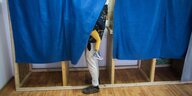 Wahlkabine mit Vorhang, hinter dem Beine mit einem Kind auf dem Arm hervorlugen