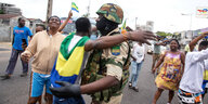 Ein Mann mit der Fahne Gabuns umgeschlungen, umarmt einen Soldaten