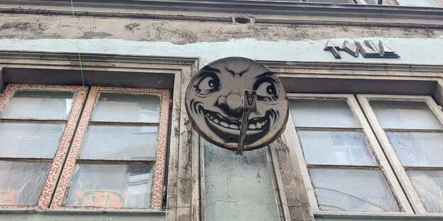 Eine mit einem lachenden Gesicht bemalte Satellitenschüssel an einer Hauswand.