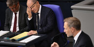 Bundeskanzler Olaf Scholz schaut von der Regierungsbank im Bundestag Christian Lindner an, der eine Rede am Pult hält. Scholz trägt eine Augenklappe, die er auf dem Bild mit seiner Hand bedeckt