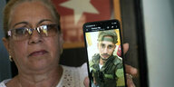 Eine Frau hält ein Smartphone hoch, das ihren Sohn in Kampfuniform zeigt