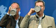 Markus Söder und Friedrich Merz trinken aus einem Bierkrug