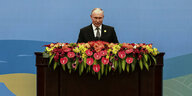 Präsident Putin steht vor einem breiten Pult, das mit Blumen behangen ist.