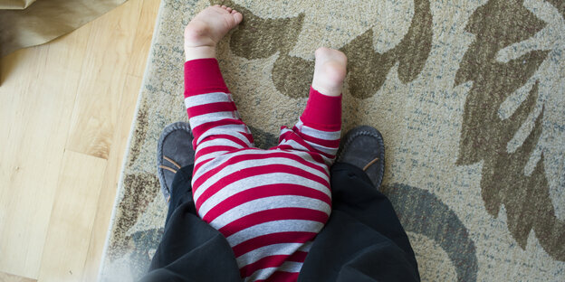 Ein Baby krabbelt zwischen den Füßen eines Erwachsenen.