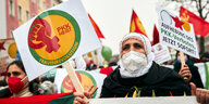Protestzug, im Vordergrund eine ältere Frau mit Gesichtsmaske und einem Schild: "PKK heisst Frauenrevolution" und dem Frauen-Symbol.