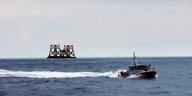 Ein Boot der US-Küstenwache vor einem Lastkahn mit Windturbinen-Plattformen