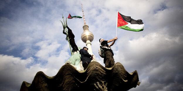 Junge Männer stehen auf dem Neptunbrunnen mi Palästina-Flaggen - im Hintergrund der Fernsehturm