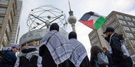 Teilnehmer einer pro-palästinensischen Kundgebung sind mit Fahnen und Pali-Tüchern auf dem Alexanderplatz unterwegs.