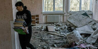 Eine Frau trägt Aktenordner aus einem mit Trümmern übersähten Raum