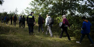 Ein Polizist eskortiert eine Reihe von Migranten in einem Wald