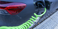 Ein E-Auto lädt Strom. Der Stecker im Fahrzeug mündet in ein giftgrünes Ladekabel, das spiralförmig in der Luft hängt