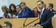 Christoph Maier steht am Rednerpult des Bayerischen Landtags, Markus Söder und andere Politker und Politekrinnen hören ihm zu. Söder verzieht das Gesicht.