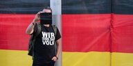 Ein Teilnehmer steht während einer Kundgebung der islam- und fremdenfeindlichen Pegida-Bewegung auf dem Wiener Platz vor einer Deutschlandflagge und hält ein Smartphone.