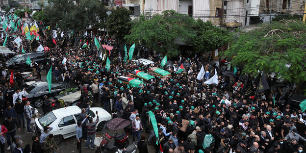 Eine Menschenmenge mit Palästina-Fahnen auf einer Staße, sie tragen Särge über ihren Köfen.