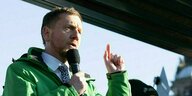 Michael Kretschmer in grüner Jacke mit Mikrofon in der Hand